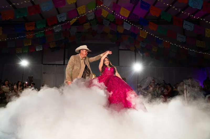 Padre e hija comparten un momento de Dance on the Clouds en una pista de baile cubierta de niebla bajo banderines de papel picado en una quinceañera de DJ Oso