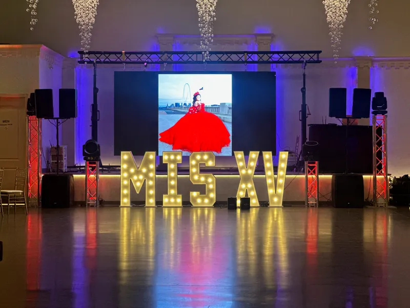 Letras luminosas MIS XV frente a una pantalla LED de video con una quinceañera en vestido rojo en la Reunion Tower de Dallas, montado por DJ Oso